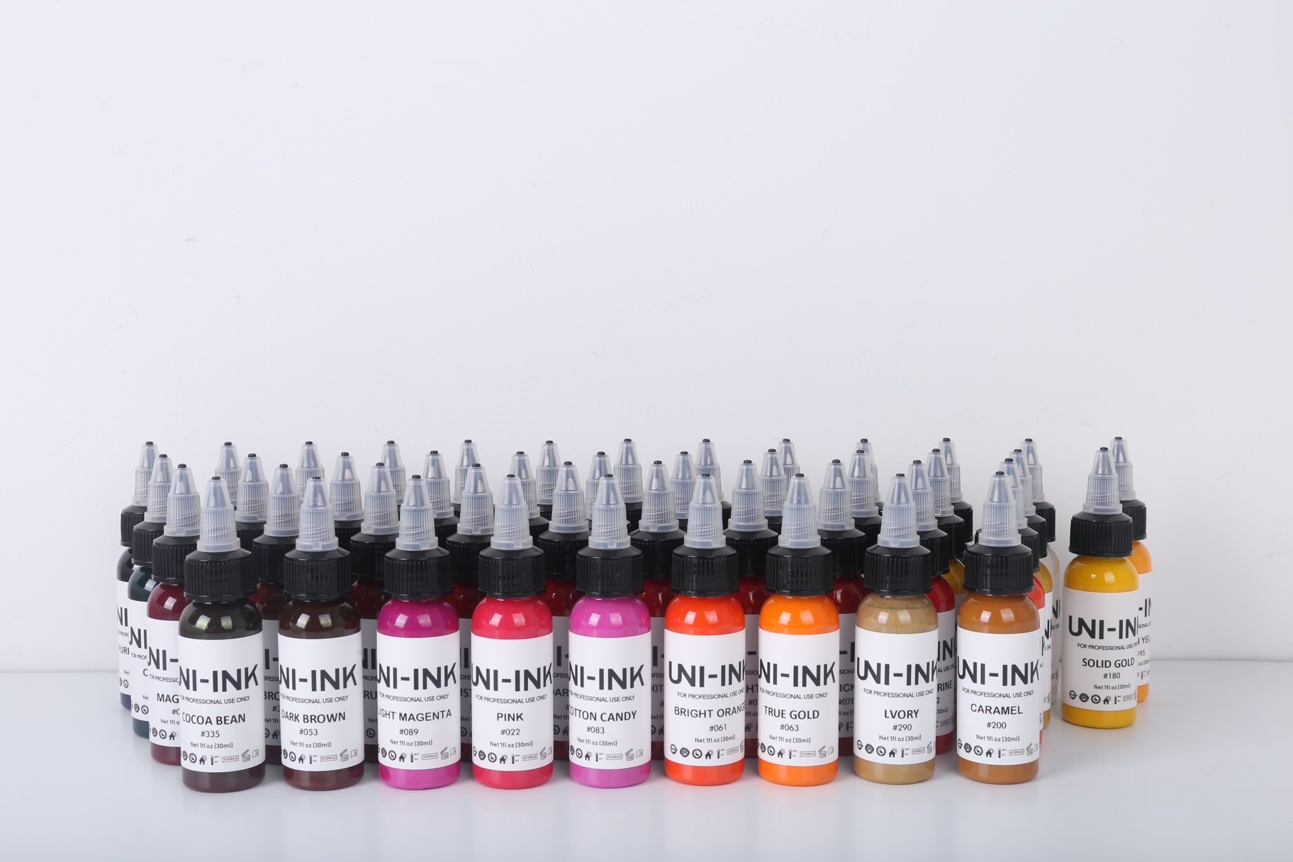 Uni-Ink professional tattoo ink bottles in multiple colours including pink, orange, brown, gold and magenta arranged in a row.